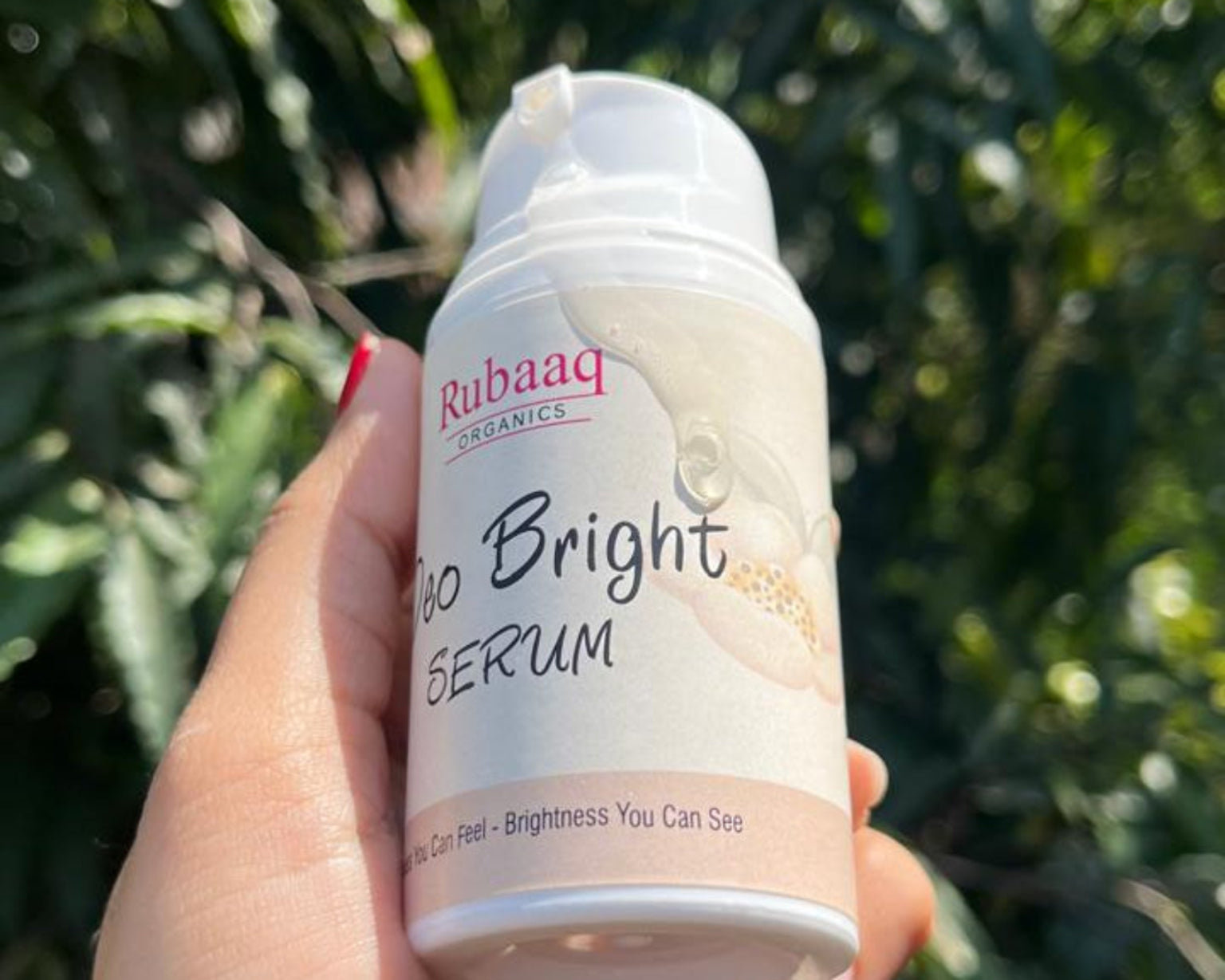 Hand holding a bottle of 'Rubaq' brightening serum against a green leafy background